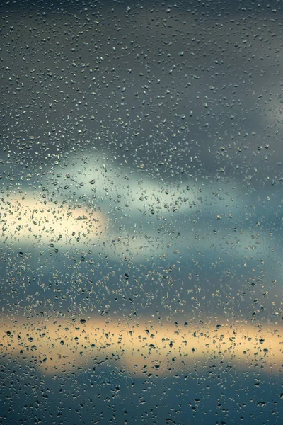 カラフルな夕日雲の背景に窓ガラスの表面に雨滴 — ストック写真