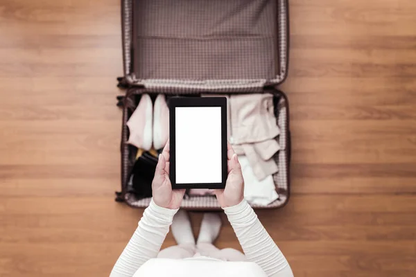 Top view of woman packing a luggage for a new journey. Female standing above suitcase with electronic note pad and cup of coffee. Space for text.