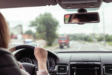 Kadın otobanda araba sürüyor. Arabanın arka koltuğundan bak. 