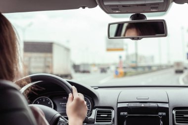 Kadın otobanda araba sürüyor. Arabanın arka koltuğundan bak. 