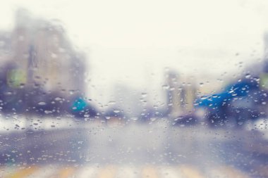 Bir kavşak ve yaya geçidinde yağmur damlaları ile bir arabanın ön camından bulanık görünümü.