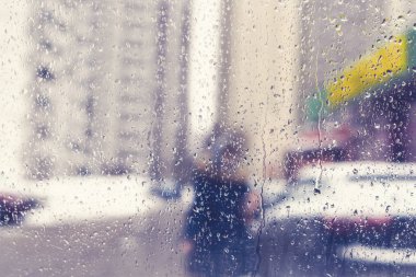 Bir kavşak ve yaya geçidinde yağmur damlaları ile bir arabanın ön camından bulanık görünümü.