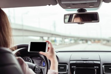 kadın karayolu üzerinde sürüş ve cep telefonu tutuyor. Arabanın arka koltuğundan görünüm
