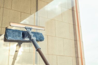 Balkon penceresini temizleyen kız temizlik ürünlerini spreyliyor ve yaz günbatımında süngerle siliyor..