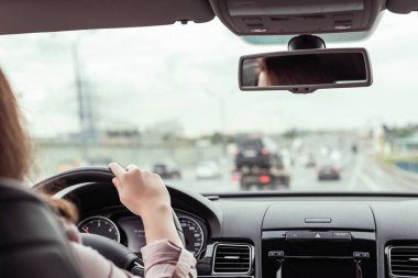 Kadın otobanda araba sürüyor. Arabanın arka koltuğundan bak. 