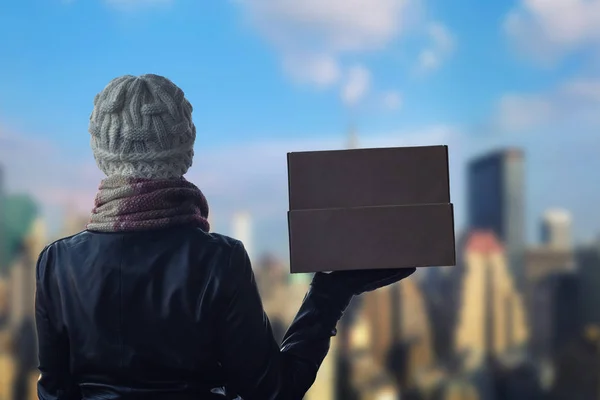 A girl in winter clothes with a box for pizza on the Manhattan background. New York city.
