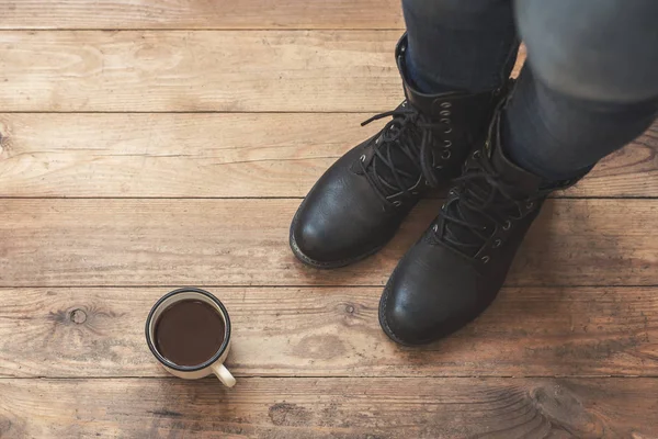 A girl in the boots with an iron mug of coffee on the terrace of a wooden house.  concept