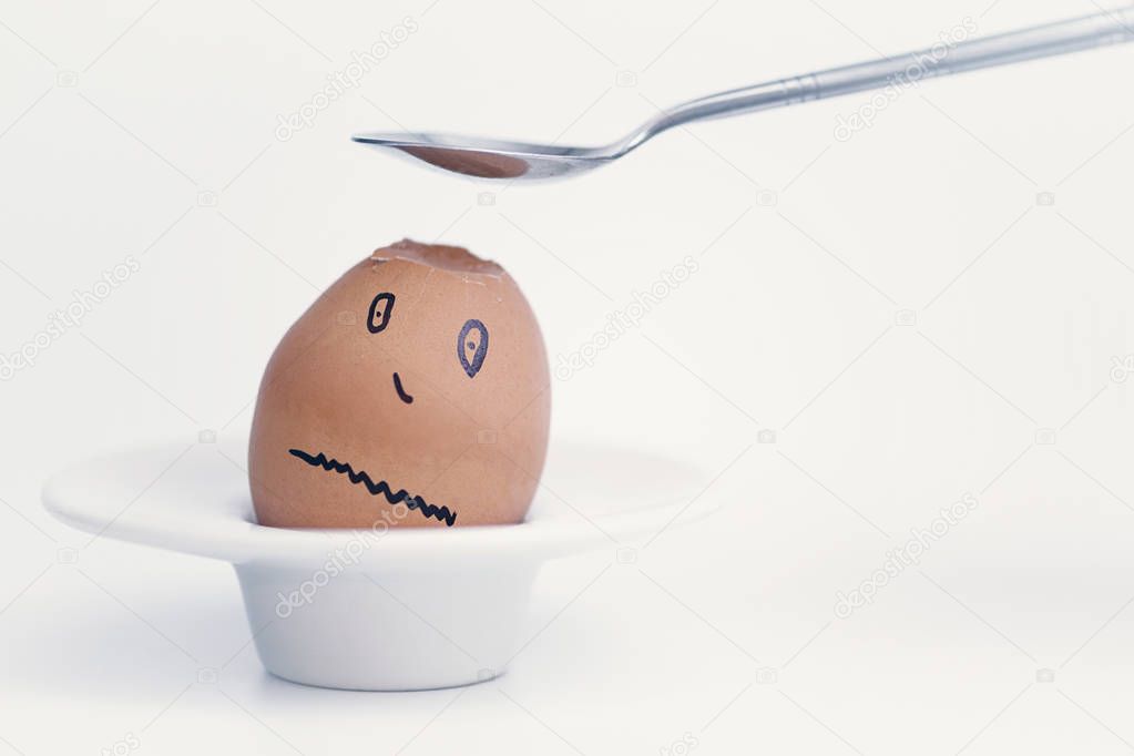 Spoon breaks sad egg on a stand in the form of human head . Concept. 