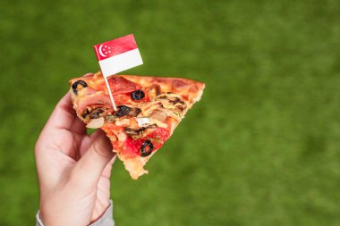 Bir kürdan şeklinde Singapur bayrağı ile kadın elinde pizza bir dilim. Yeşil çimenlerin üzerinde öğle yemeği. Çin. Kavram