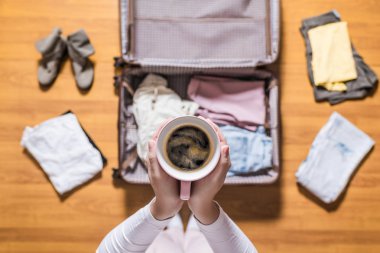 Yeni bir yolculuk için bir bagaj ambalaj ve pembe fincan kahve içme kadın elleri üst görünümü . 