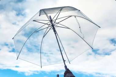 Bulutlu gökyüzü arka plan üzerinde yağmurlu bir sonbahar gününde şeffaf bir şemsiye ile Kadın el