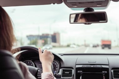 Kadın otobanda araba sürüyor. Arabanın arka koltuğundan bak. 