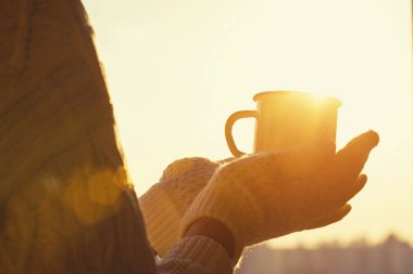 Gün batımı gökyüzüne karşı bir kış soğuk bir günde örme eldivenler kadın elinde sıcak çay ile Demir kupa