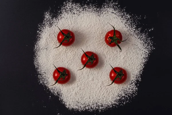 A pizza drawing on a black background made from flour and tomatoes. Concept