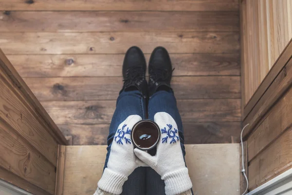 A girl in the boots with an iron mug of coffee on the terrace of a wooden house. Winter concept