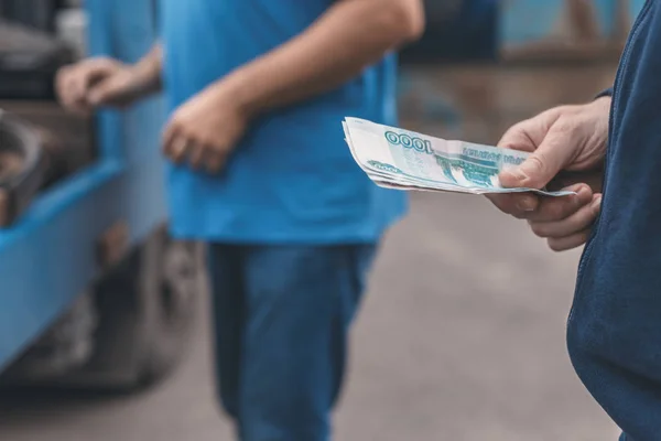 Man pays paper money for tow truck to worker towing a broken down car. Selective focus. Concept