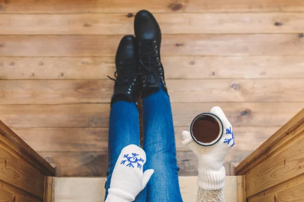 A girl in the boots with an iron mug of coffee on the terrace of a wooden house. Winter concept