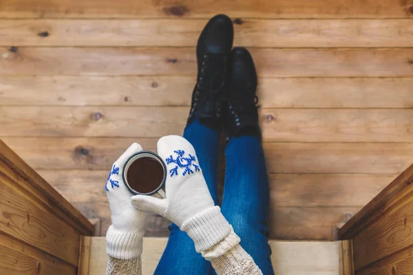 A girl in the boots with an iron mug of coffee on the terrace of a wooden house. Winter concept