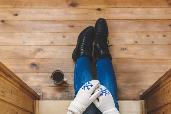 A girl in the boots with an iron mug of coffee on the terrace of a wooden house. Winter concept