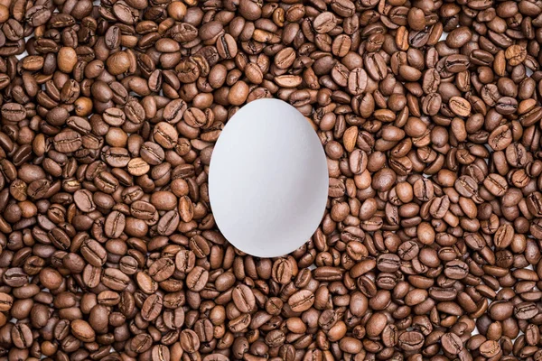 新鲜烤咖啡豆背景上的白蛋 创意复活节概念 — 图库照片