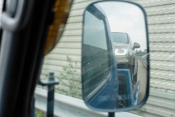 View from car side mirror of tow truck towing a broken down car on the highway