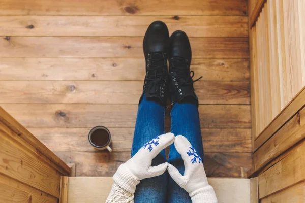 A girl in the boots with an iron mug of coffee on the terrace of a wooden house. Winter concept