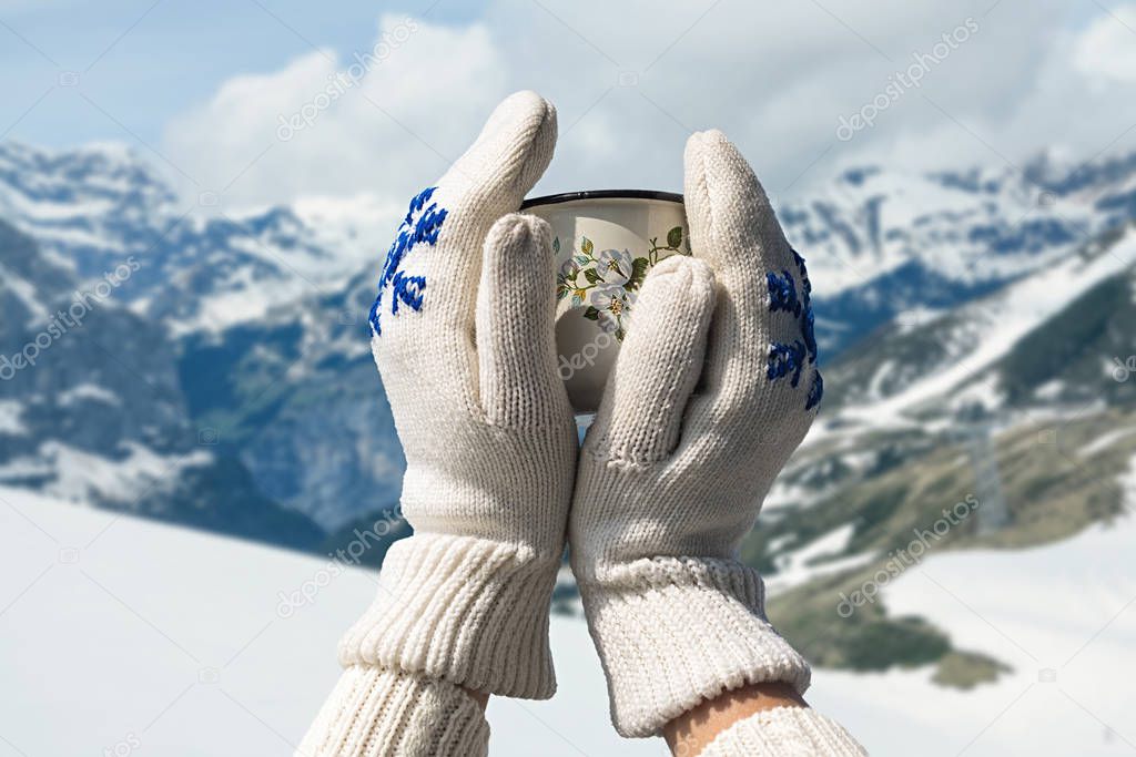 Iron mug with hot tea in female hands in knitted mittens in a winter frosty day 