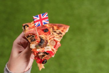 Dişdan şeklinde İngiliz bayrağı olan kadın ellerinde bir dilim pizza. Yeşil çimenlerin üzerinde öğle yemeği. Ingiltere. Kavram