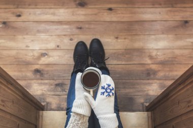 Ahşap bir evin terasında demir bir fincan kahve içen çizmeli bir kız. Kış konsepti