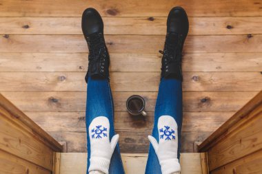 Ahşap bir evin terasında demir bir fincan kahve içen çizmeli bir kız. Kış konsepti