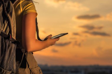 şort ve bir sırt çantası ve gün batımı arka plan üzerinde tablet ile bir t-shirt kadın yürüyüşçü