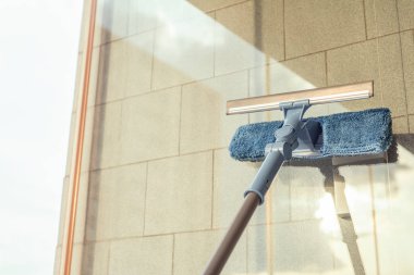 Balkon penceresini temizleyen kız temizlik ürünlerini spreyliyor ve yaz günbatımında süngerle siliyor..