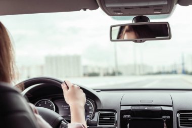 Kadın otobanda araba kullanıyor. Arabanın arka koltuğundan görünüm 