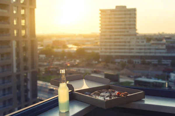 huge pizza in a box with a bottle of mojito on the sunset city background