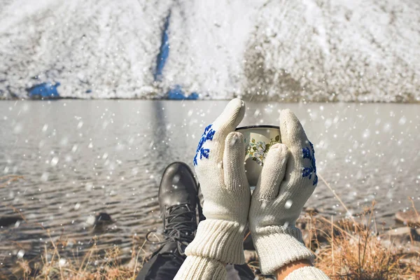 Iron mug with hot tea in female hands in knitted mittens in a winter frosty day on  background