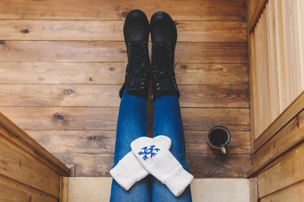 A girl in the boots with an iron mug of coffee on the terrace of a wooden house. Winter concept