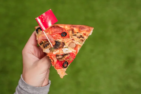 つまようじの形で中国の旗を持つ女性の手のピザのスライス 緑の草の上で昼食 — ストック写真