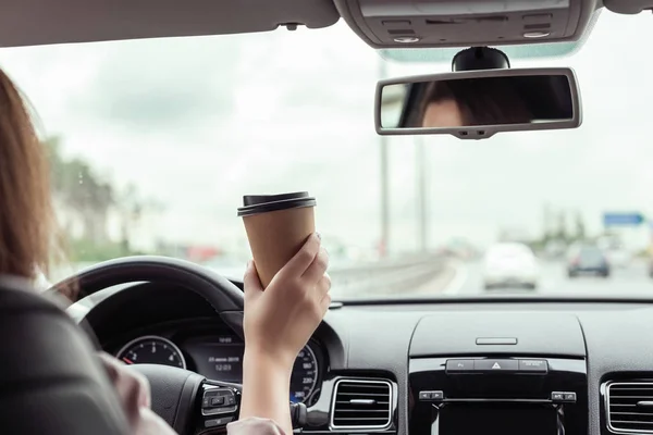 女性はオートバーンで運転し 朝にコーヒーの紙コップを持っています 車の後部座席からの眺め — ストック写真