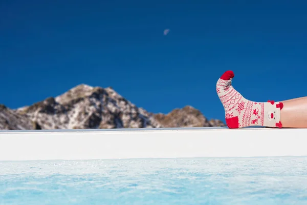 Women\'s feet in Christmas socks near the pool on the Swiss Alps background. Winter concept.