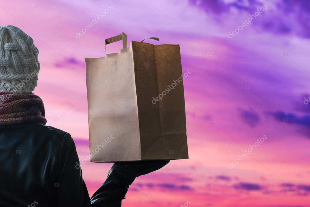 A woman in a winter clothes with a paper bag on the background of the evening city. 24 hours delivery. Concept