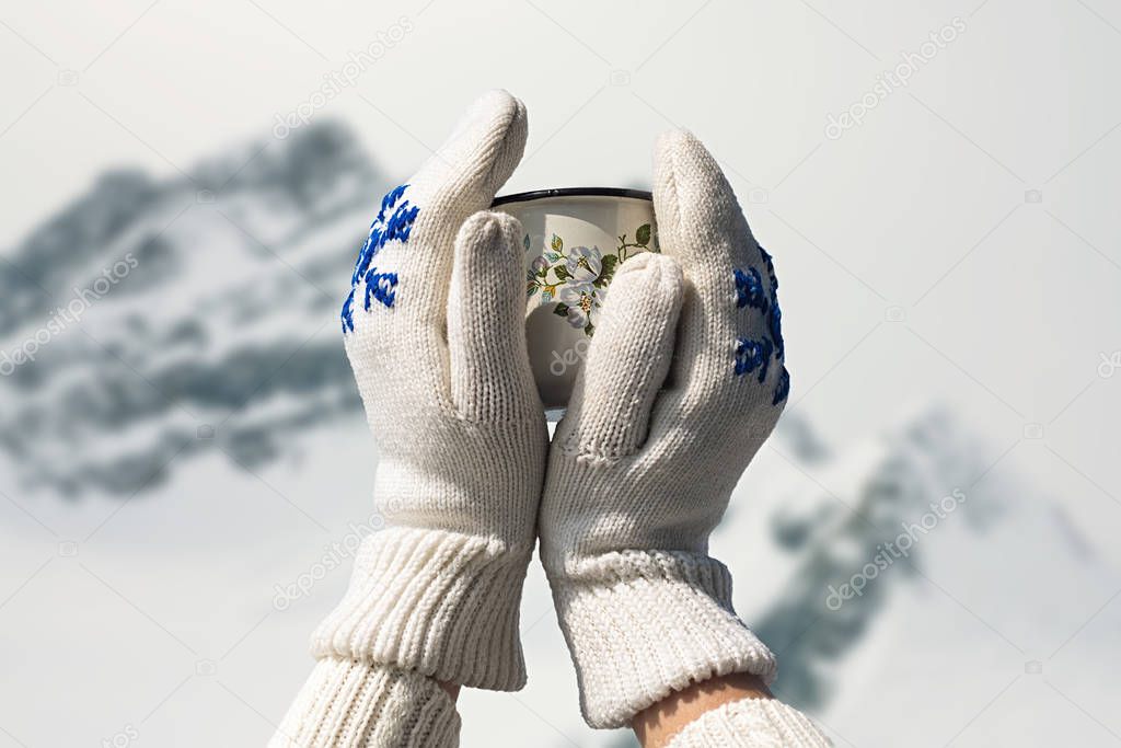 Iron mug with hot tea in female hands in knitted mittens in a winter frosty day on  background