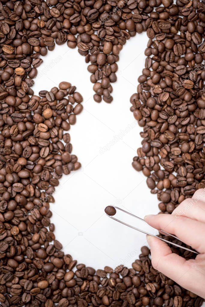 Female hand with tweezers laying out coffee beans and creates the shape of an Easter bunny. Creative concept