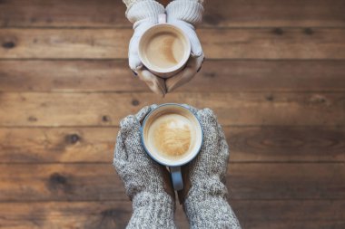 Kışın erkek ve dişi nin elleri ahşap masa arka planda bir fincan kahve ile eldiven örülmüş. Kış konsepti