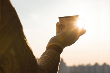 Gün batımı gökyüzüne karşı bir kış soğuk bir günde örme eldiven kadın elinde sıcak çay ile Demir kupa
