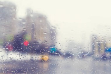 Bir kavşak ve yaya geçidinde yağmur damlaları ile bir arabanın ön camından bulanık görünümü.