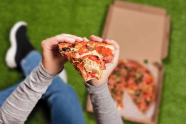 Kadın ellerinde bir dilim pizza. Yeşil çimenler üzerinde öğle yemeği