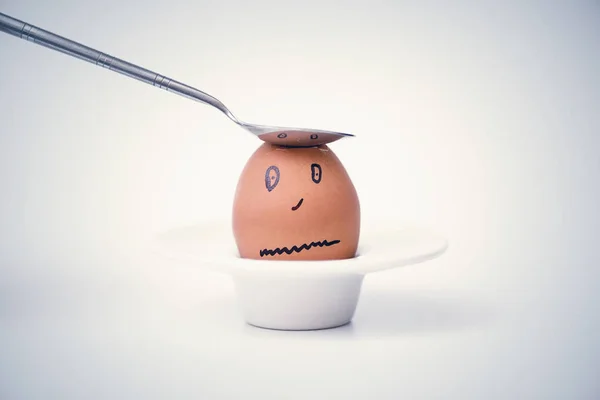 Spoon breaks sad egg on a stand in the form of human head . Concept.