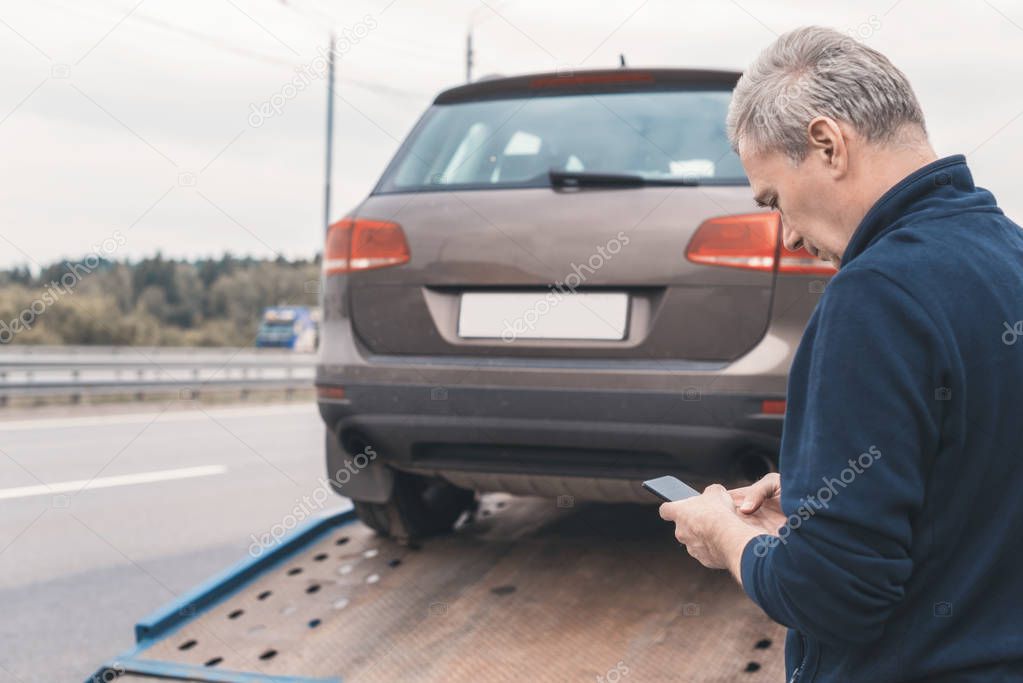 Man with mobile phone.Tow truck with worker towing a broken down car on the highway. Selective focus. Concept