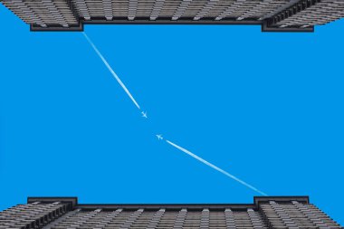 Uçaklar iki bina arasında açık mavi gökyüzünde izler bırakıyor. 