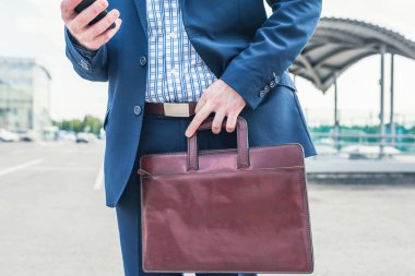 Takım elbiseli sıska adam sokakta telefonla ararken gömleğini pantolonuna sokuyor..